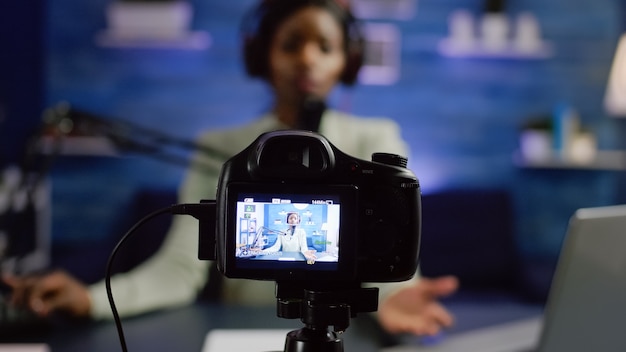 Afrykański blog influencer nagrywający, patrzący na profesjonalną kamerę w domowym studiu online talk show