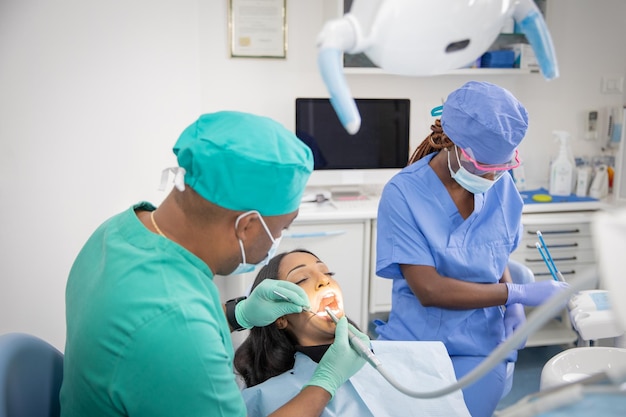 Afrykański dentysta sprawdza stan jamy ustnej swojego pacjenta, podczas gdy jego asystent przygotowuje narzędzia pracy