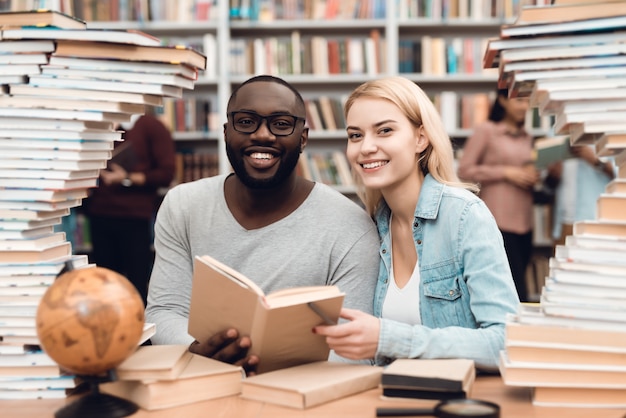 Afrykański facet i biała dziewczyna otaczający książkami w bibliotece.