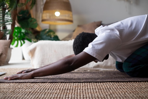 Afrykański mężczyzna robi jogę w domu po lekcji jogi, odpoczywa w balasanie lub pozie dziecka