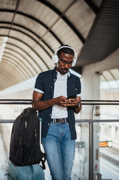 Afrykański mężczyzna używający telefonu i słuchający muzyki na stacji kolejowej