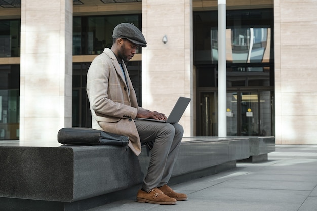 Afrykański młody biznesmen pisania na laptopie, który pracuje online, siedząc w mieście