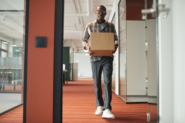 Afrykański młody człowiek niosący pudełko z rzeczami, idąc korytarzem biura, dostaje nową pracę