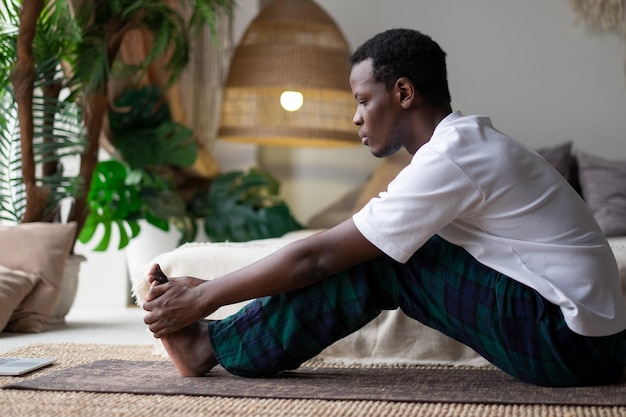 Afrykański młody mężczyzna siedzący w pozie paschimottanasana lub Intense Dorsal Stretch