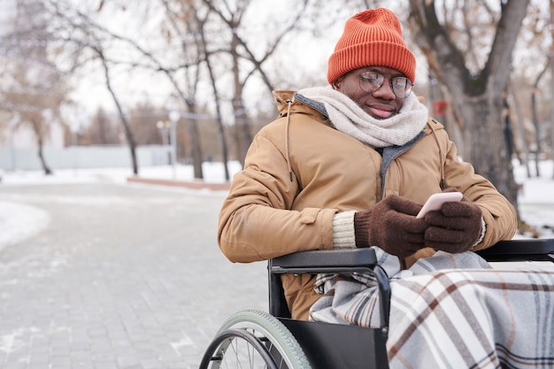 Afrykański Niepełnosprawny Mężczyzna Piszący Wiadomość Na Telefonie Komórkowym Siedząc Na świeżym Powietrzu W Zimowy Dzień