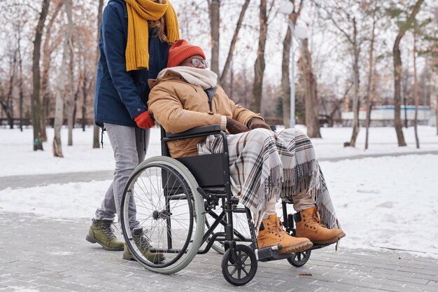 Afrykański niepełnosprawny mężczyzna siedzący na wózku inwalidzkim w zimowy dzień razem ze swoim asystentem