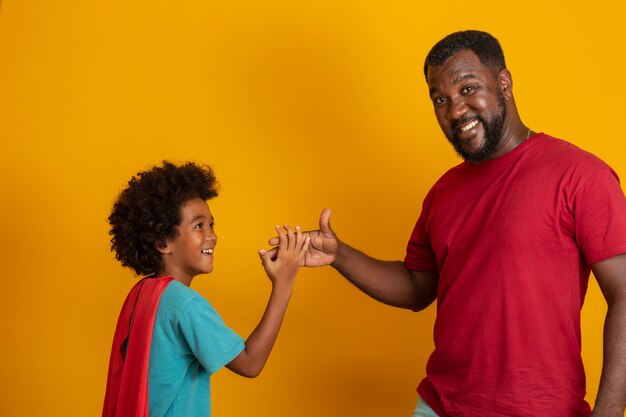 Afrykański Ojciec I Syn Grający W Superhero W Czasie Dnia. Ludzie Zabawy żółtą ścianę. Pojęcie Przyjaznej Rodziny.
