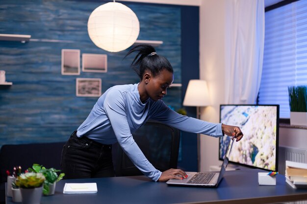 Afrykański przedsiębiorca pracujący w domu późno w nocy przy użyciu laptopa do pracy nad ważnym projektem. Czarny przedsiębiorca siedzi w osobistym miejscu pracy pisania na klawiaturze.