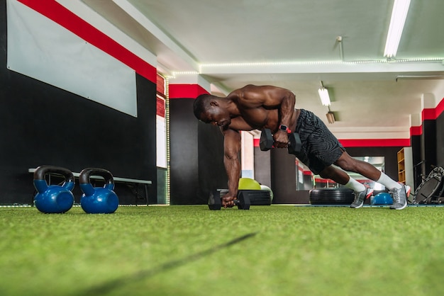 Afrykańskich kulturystów mężczyzna sportowiec robi triceps tonujące ćwiczenia z kettlebells w siłowni. Afrykański kulturysta ćwiczący crossfit rutynowo bez koszulki na siłowni