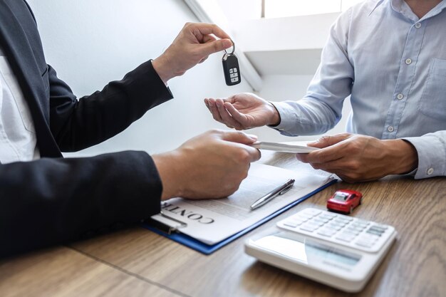 Zdjęcie agent daje klientowi klucz do samochodu za pomocą papierów i waluty na stole