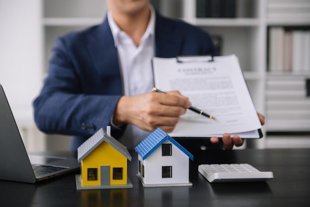 Agent pośrednika w obrocie nieruchomościami przedstawiający klientowi do podejmowania decyzji znak umowy ubezpieczenia kupna i sprzedaży modelu domu dotyczącego oferty kredytu hipotecznego