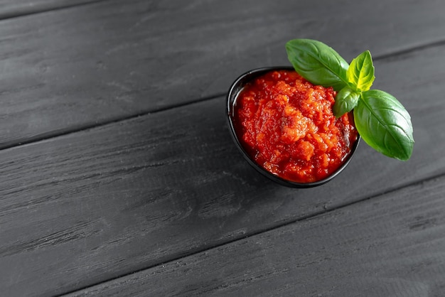 Ajvar w czarnym flakonie z bazylią na drewnianym czarnym tle pasta ze słodkiej papryki