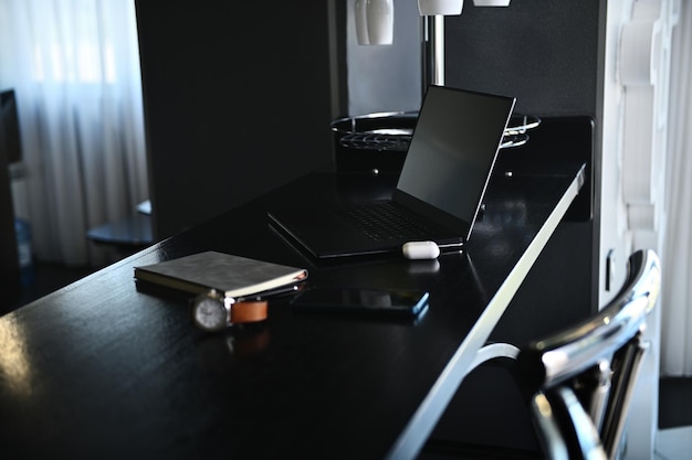 Akcesoria biurowe, artykuły papiernicze, laptop, słuchawki na pudełku, zegarek, telefon komórkowy i szary notatnik na drewnianym stole w domowej kuchni