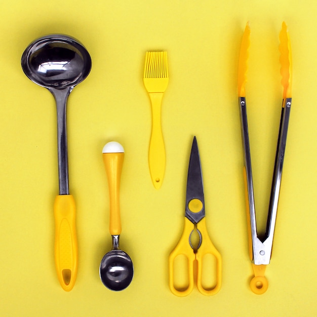 Akcesoria do kadzi kuchennych, nożyczki, szczypce, pędzel, żółta łyżka do lodów na żółtym tle