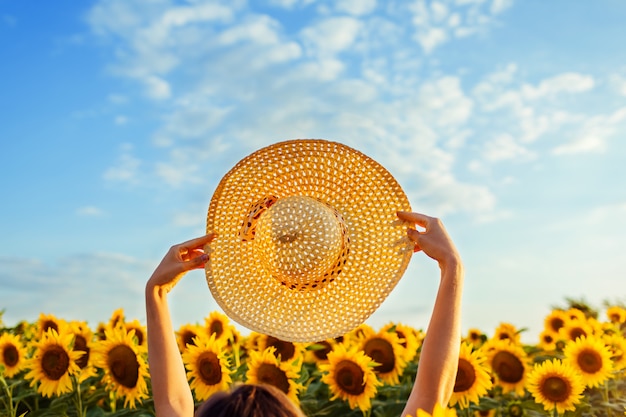 Akcesoria do letnich wakacji. Kobiety odprowadzenie w kwitnącym słonecznika polu podnosi kapelusz