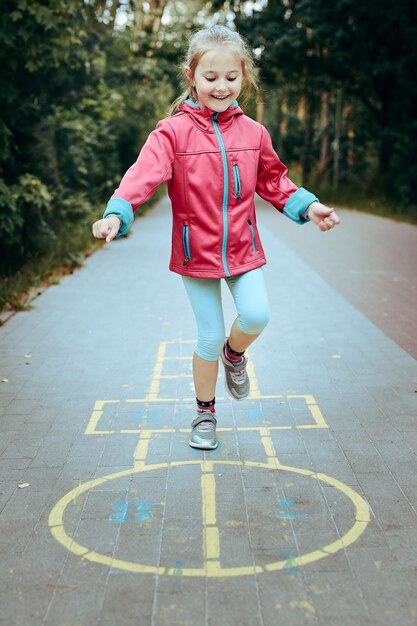 Zdjęcie aktywna dziewczynka bawiąca się w hopscotch na placu zabaw na świeżym powietrzu skacząca z radości aktywność dzieci