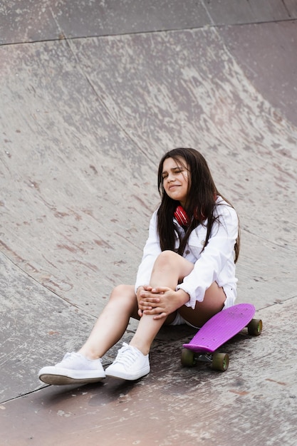 Aktywna dziewczynka po upadku z deski grosza ranna siedząca i patrząca na siniaka na rampie sportowej na placu zabaw w skateparku