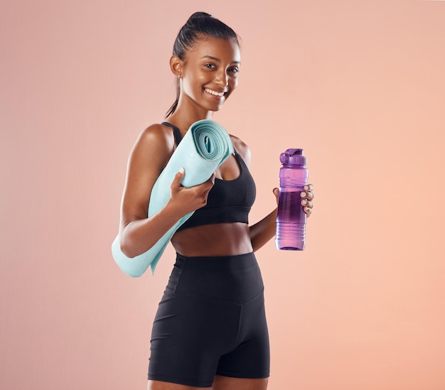 Aktywna kobieta przygotowuje się do rutynowego treningu fitness, trzymając matę do jogi i butelkę, stojąc na różowym tle studio