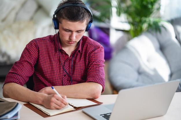 Aktywna nastolatka ze słuchawkami słucha wykładu, robi w notebooku, używając laptopa