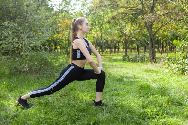 Aktywna sprawna kobieta w stroju sportowym ćwiczy ćwiczenia rozciągające w parku w jasny słoneczny dzień Koncepcja fitnessu zdrowego stylu życia