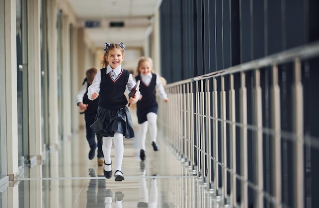 Aktywne dzieci szkolne w mundurkach biegających razem po korytarzu Koncepcja edukacji