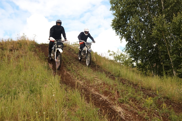 Aktywni motocykliści w kaskach jadący na motocyklu z górki, rozwijający swoje umiejętności na torze terenowym