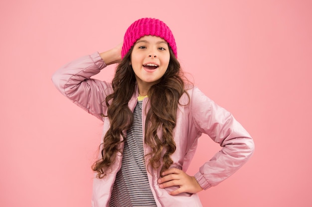 Aktywności zimowe mała dziewczynka kurtka puchowa i czapka z dzianiny opieka zdrowotna w chłodne dni dobry nastrój w każdą pogodę dziecko w ciepłych zimowych ubraniach sezonowa moda dla dzieci mała uroda różowa ściana