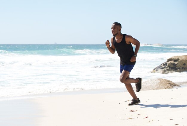 Aktywny amerykanina afrykańskiego pochodzenia mężczyzna bieg wodą przy plażą
