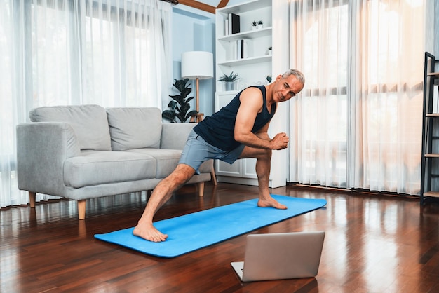 Aktywny i sprawny starszy mężczyzna rozgrzewka i rozciąganie przed ćwiczeniami w domu w salonie podczas oglądania wideo fitness w Internecie Koncepcja zdrowego stylu życia po przejściu na emeryturę dla emeryta Clout