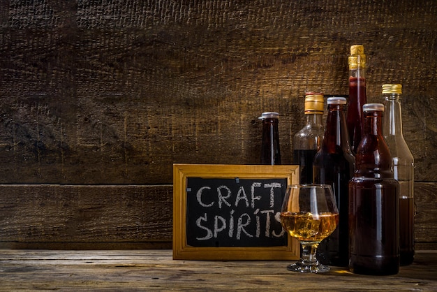 Alkohol spirytusowy rzemieślniczy Różne butelki i szkło z ręcznie wykonanymi mocnymi napojami alkoholowymi Stare drewniane rustykalne tło
