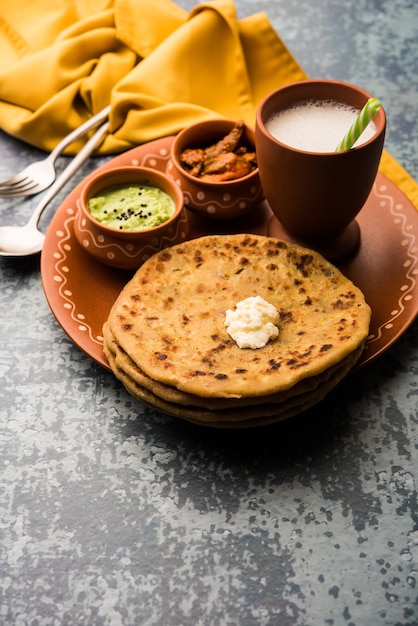 Aloo Paratha lub Indian Potato Faszerowane Flatbread z masłem na wierzchu. Podawany ze świeżym słodkim lassi, chutneyem i piklami. selektywne skupienie