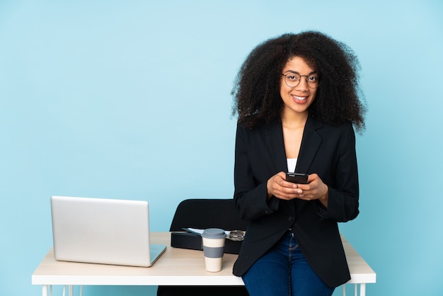 Amerykanin afrykańskiego pochodzenia biznesowa kobieta pracuje w jej miejscu pracy wysyła wiadomość z wiszącą ozdobą