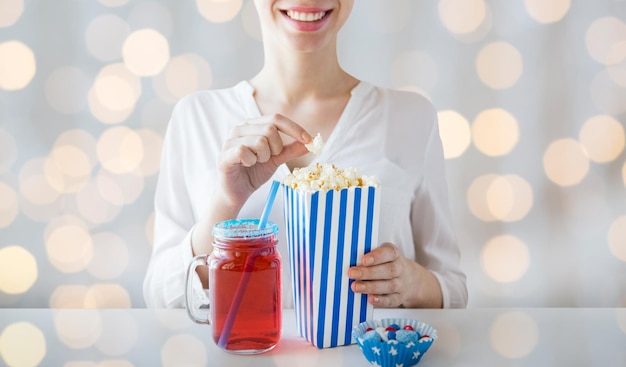 Zdjęcie amerykański dzień niepodległości, celebracja, patriotyzm i koncepcja wakacji - zbliżenie kobiety jedzącej popcorn z napojem w szklanym słoiku mason i cukierki na imprezie 4 lipca na tle światła