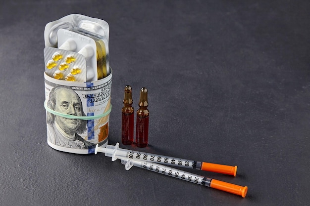 Ampułki do tabletek i strzykawki zawinięte w banknoty dolarowe zapinane na gumkę na czarnym tle