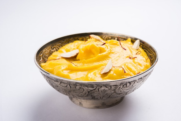 Amrakhand to jogurt o smaku Alphonso lub Shrikhand, popularne indyjskie słodycze podawane z suszonymi owocami i szafranem z całymi owocami mango, na kolorowym tle. selektywne skupienie