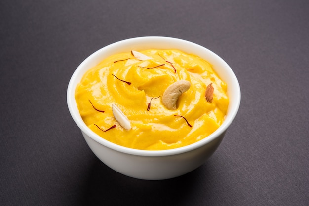 Amrakhand to jogurt o smaku Alphonso lub Shrikhand, popularne indyjskie słodycze podawane z suszonymi owocami i szafranem z całymi owocami mango, na kolorowym tle. selektywne skupienie