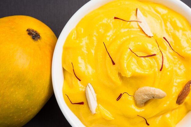 Amrakhand to jogurt o smaku Alphonso lub Shrikhand, popularne indyjskie słodycze podawane z suszonymi owocami i szafranem z całymi owocami mango, na kolorowym tle. selektywne skupienie