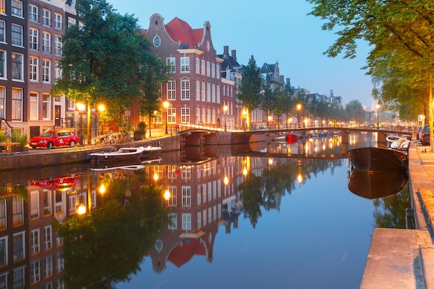 Amsterdam kanał Kloveniersburgwal z typowymi holenderskimi domami, mostem i łodziami mieszkalnymi podczas porannej niebieskiej godziny, Holandia, Holandia.