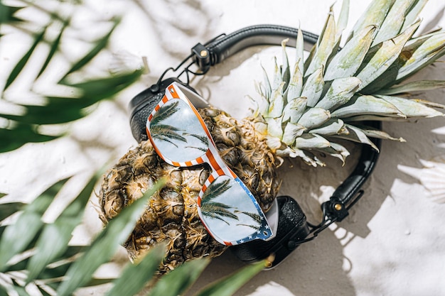 Ananas w okularach przeciwsłonecznych i słuchawkach na tropikalnej plaży nad morzem lub oceanem na wakacjach