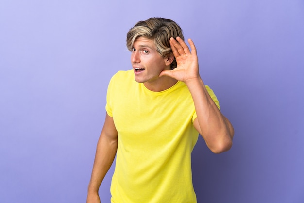Angielski człowiek nad odosobnioną fioletową ścianą słuchając czegoś, kładąc rękę na uchu