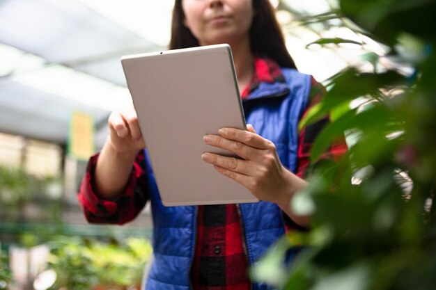 Anonimowa kobieta pracująca w szklarni sprawdzająca rośliny za pomocą tabletu