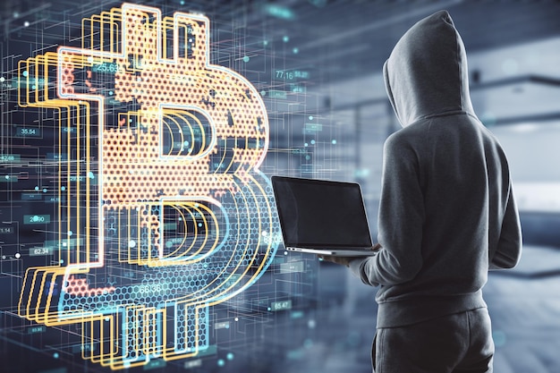 Anonimowy rynek finansowy i koncepcja kryptowaluty z człowiekiem w bluzie z kapturem za pomocą laptopa z tyłu przed cyfrowym ekranem z symbolem bitcoin z plastrami miodu wewnątrz na niewyraźne tło biurowe