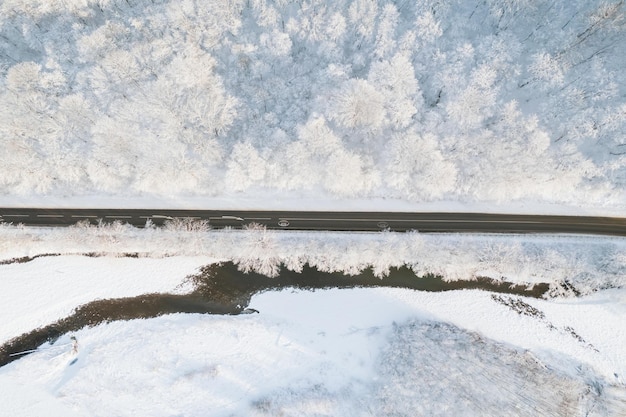 Antena z góry na dół filmowa zima zaśnieżona wiejska droga asfaltowa serpentyna Samochody jeżdżą wśród lasów
