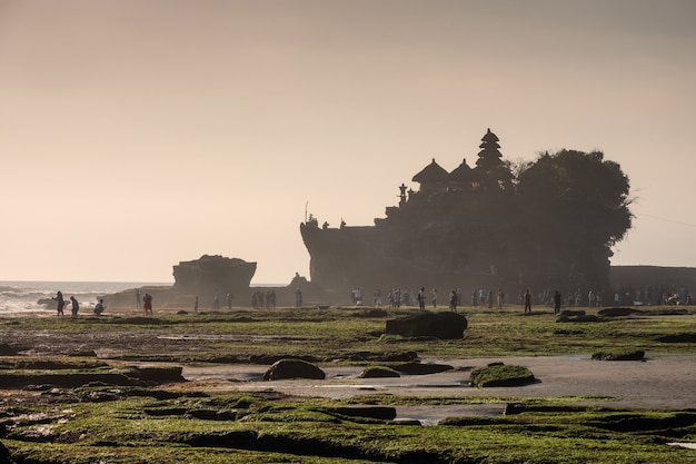 Antyczna Tanah Lot świątynia z marzycielskimi turystami na linii brzegowej