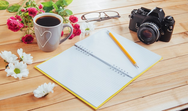 Aparat fotograficzny, okulary, notatnik i ołówek na brązowym drewnianym