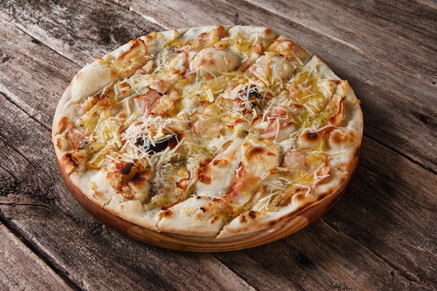 Apetyczna gorąca pizza pieczona z serem, boczkiem i szynką podawana na drewnianym stole w stylu rustykalnym. Włoskie fast foody, tradycyjna kuchnia.