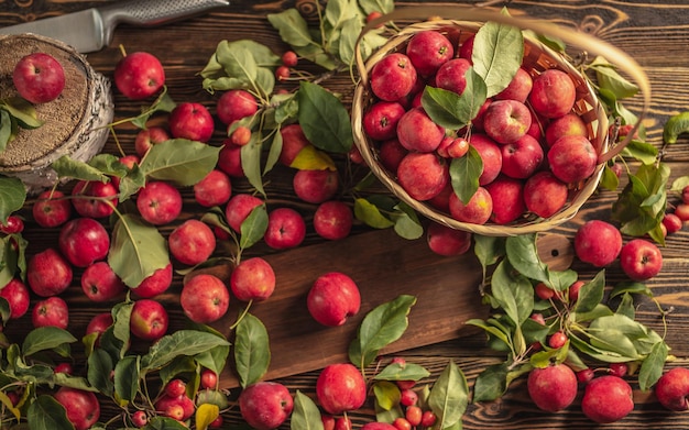 Apetyczne czerwone jabłka z zielonymi liśćmi na drewnianym stole i w koszu Świeże zbiory i jesienny nastrój