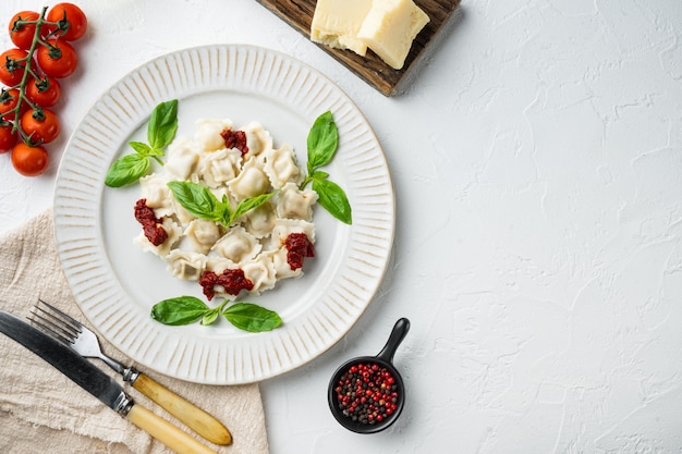 Apetyczne ravioli z sosem pomidorowym, serem i bazylią zestaw z bazyliowym parmezanem i pomidorem na białym talerzu, na białym tle, widok z góry na płasko, z copyspace i miejscem na tekst