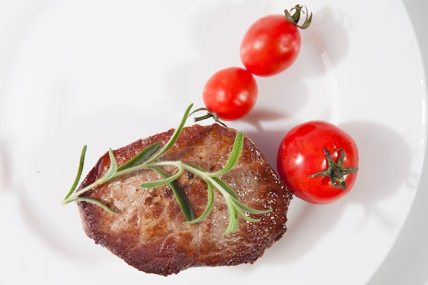 Apetyczny stek dobrze wysmażony na białym talerzu z pomidorami i rozmarynem