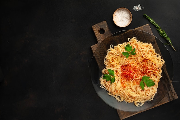 Apetyczny włoski makaron spaghetti z sosem pomidorowym, parmezan na talerzu, deska do krojenia na betonowym tle. Widok z góry